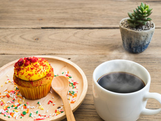 Yellow cupcakes put on a spherical wooden plate. Beside of cupcake have Cactus and white coffee mug.All of it rests on wooden table.