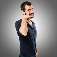 Handsome man with beard making phone gesture on grey background