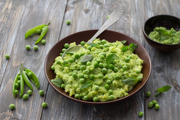 Mashed potatoes with green peas, mint and olive oil in a ceramic bowl on a wooden table. Healthy vegetarian food © olepeshkina