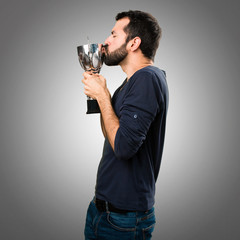 Handsome man with beard holding a trophy on grey background
