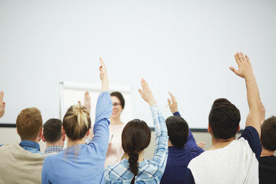 Enthusiastic Group Of Students Sitting In Classroom With Raised Hands