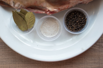 Carp with scales peeled and prepared for cooking, with spices on a white plate.