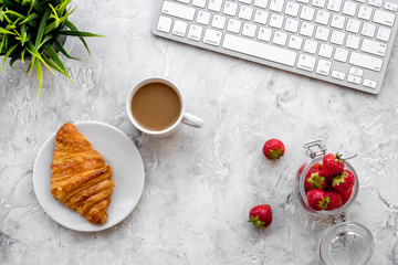 Dessert fo light lunch at workplace. Coffee, strawberry, croissant near keyboard on grey background top view copyspace