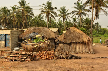 House & barracks with thatched roof with household items in a yard with palm trees in background. Rural lifestyle of West Africa. Traditional way of life in developing countries. Ghana