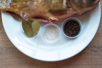 Carp with scales peeled and prepared for cooking, with spices on a white plate.