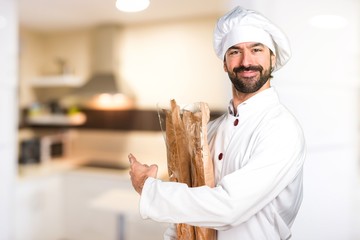 Young baker holding some bread and pointing back in the kitchen