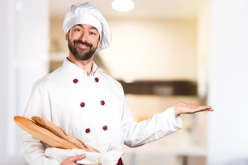 Young baker holding some bread and presenting something in the kitchen