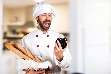 Young baker holding some bread and holding vintage clock in the kitchen