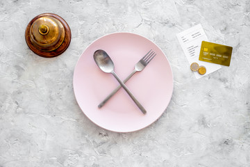 Meal is over. Bill and bank card near plate with crossed spoon and fork on grey stone table top...