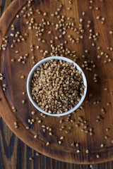 Buckwheat grain on ceramic bowl over wooden table.