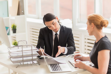 Group of confident business people discussing charts and graphs showing work results while having working meeting at spacious open plan office