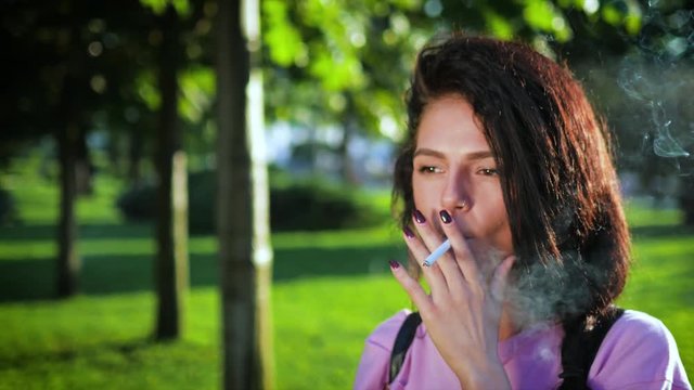 A young Сaucasian  lady is smoking a cigarette on the street.