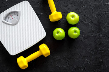 Sport and diet for losing weight. Bathroom scale, apple and dumbbell on black background top view copyspace