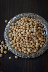 Soybeans in metal plate over black wooden background.