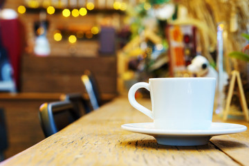 side view of espresso coffee in white cup on wooden table with blurred cafe background. copy space for text.