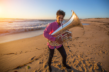 Young musician play the trumpet on rocky sea coast during surf. Tuba instrument.