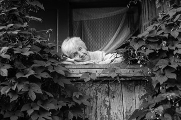 An elderly woman in the porch among the bushes.