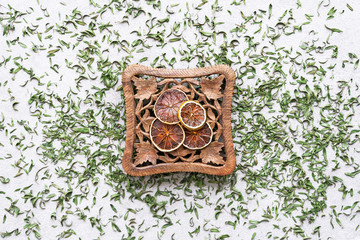 Vintage carved coaster with dry lemon slices on green tea leafs background.