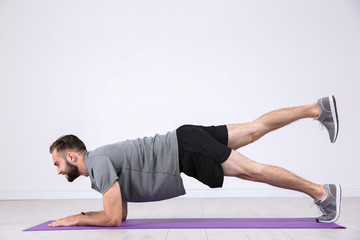 Fototapeta premium Sporty young man training legs on mat in gym