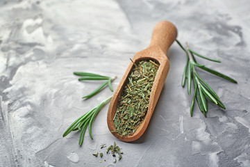 Wooden scoop with dried herbs and fresh rosemary on table