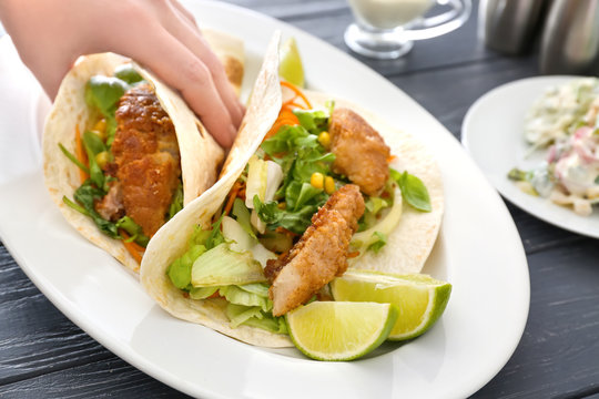 Hand taking delicious fish taco from white plate