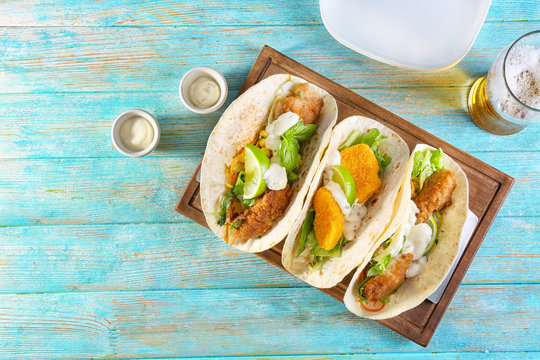 Delicious fish tacos on wooden board on blue background