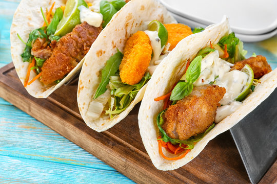 Delicious fish tacos on wooden board on blue background