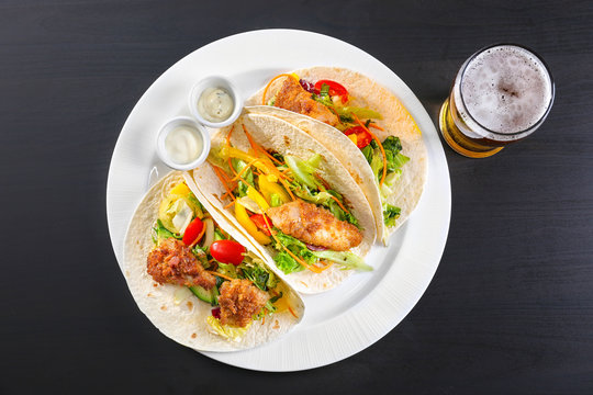 Delicious fish tacos on white plate  with beer on black background