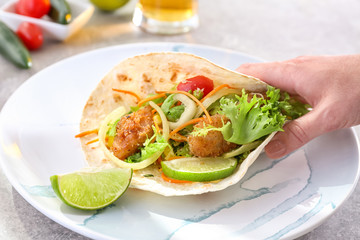 Hand taking delicious fish taco on plate on grey table