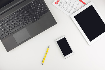 Top View Of White Office Desk With Laptop, Tablet, Smart Phone, Calendar Sheets And Supplies 