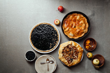 Variety of autumn pies: blueberry tart, chantarelle galette and classical apple pie with sweet pastry crust. Harvest time baking concept. Concrete rustic background. Space for text.