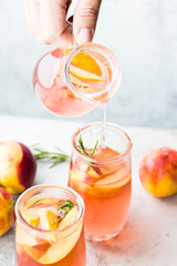 Peach and rosemary lemonade, cocktail on a gray stone concrete background. The man pours lemonade out of the pitcher. Summer drink