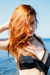 Portrait of young redhead woman wearing stylish bikini and posing on ocean background.