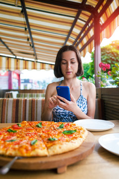 The girl is making pizza photos on the phone.