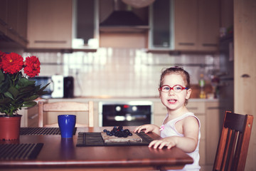 The girl sits on a chair at the table and eats berries.