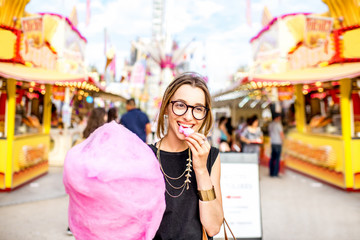 Young woman walking with pink cotton candy outdoors at the amusement park