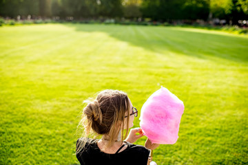 Obraz premium Young woman with pink cotton candy sitting back outdoors at the park