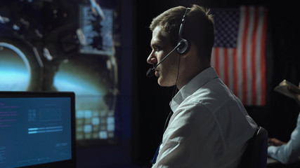 Side view of supervisor man in headset sitting and working in space mission control center. Moon...