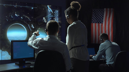 Back view of man pointing and showing to woman in space flight control center. Moon landing of...