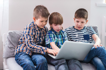 Children at home sitting on sofa, playing with laptop