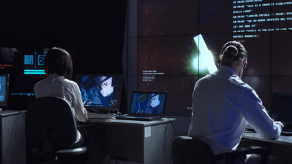 Back view of man and woman in space flight control center. Docking of space modules. Elements of this image furnished by NASA.