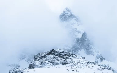 Zelfklevend Fotobehang Peak of snowy mountain surrounded by fog and clouds © Jakub Škyta