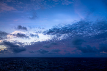 Sunset and dramatic set of clouds drifting over the tropical waters of the Caribbean Sea are lit by the last moments of daylight.