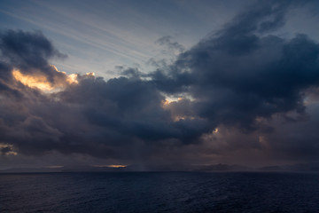 Sunset and dramatic set of clouds drifting over the tropical waters of the Caribbean Sea are lit by the last moments of daylight.