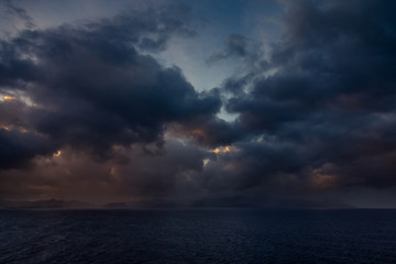 Fototapeta premium Sunset and dramatic set of clouds drifting over the tropical waters of the Caribbean Sea are lit by the last moments of daylight.