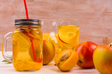 Ice tea with peaches and apples on a rustic wooden background. Detox water from fresh fruit.