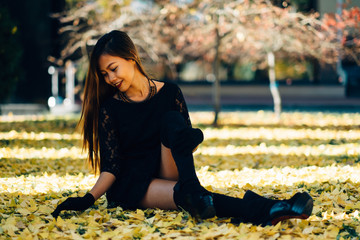 Happy young woman in park on sunny autumn day, laughing, playing leaves. Cheerful beautiful girl in black retro dress autumn fashion style