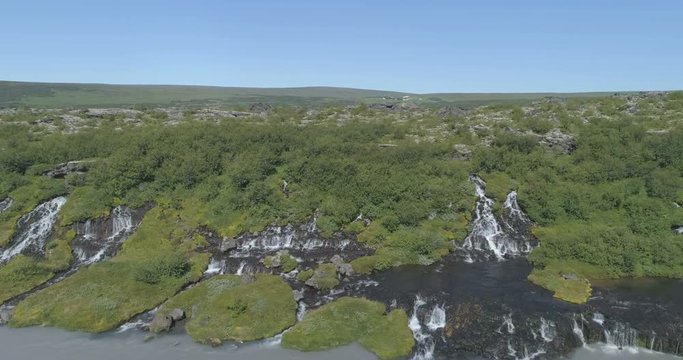 Flying diagonally over Hraunfoss lava spring waterfall glacial river Iceland aerial 4k