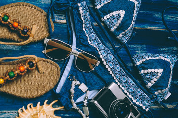 Flat lay of summer fashion with blue bikini swimsuit, camera and other girl accessories on blue wooden  background