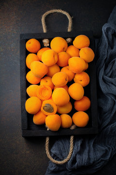 Delicious ripe apricots on a wooden stand on a dark black background. Selective focus. Top view. Cope space.